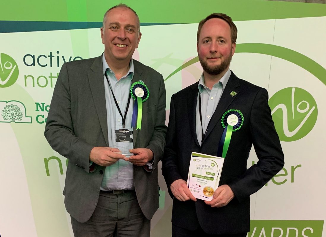 Two men standing holding an award and certificate celebrating an award win.