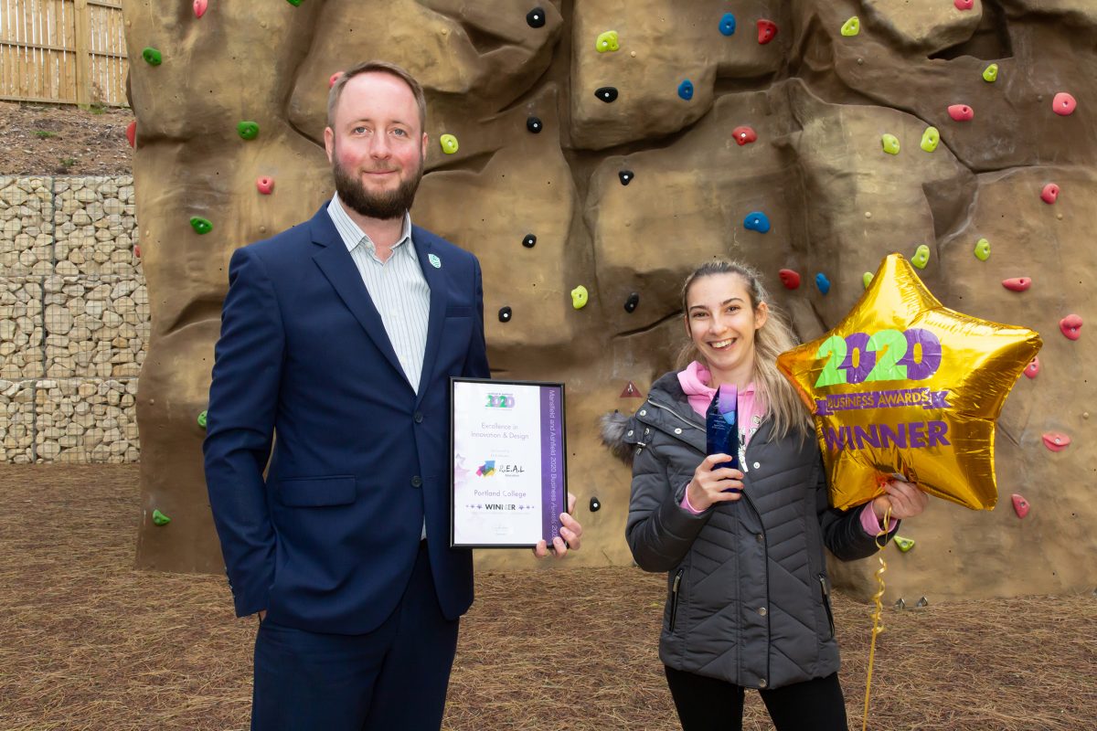 A man holding a certificate, and a girl holding a balloon standing in front of a climbing wall.