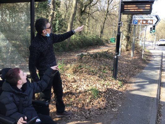Man standing and man in wheelchair pointing at bus stop