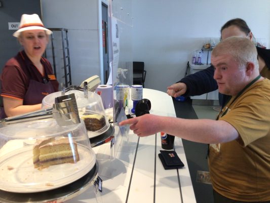 Main with blonde hair pointing at cake on cafe display.