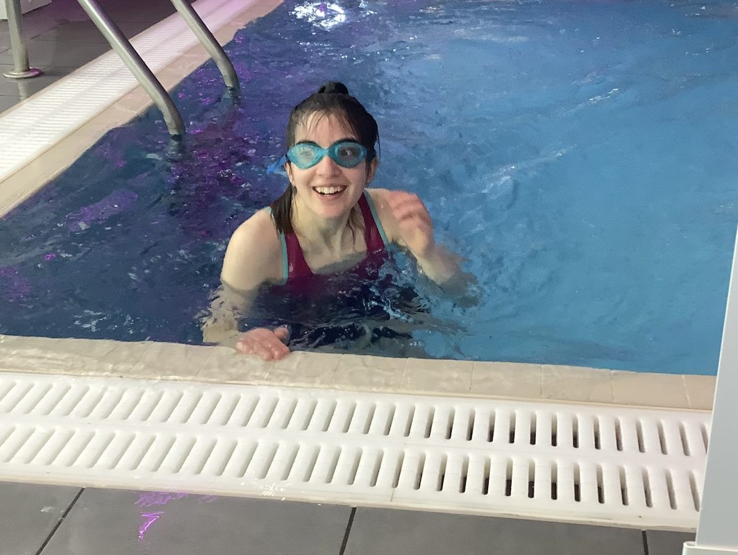 Female in a swimming pool with goggles on her facesmiling at the camera