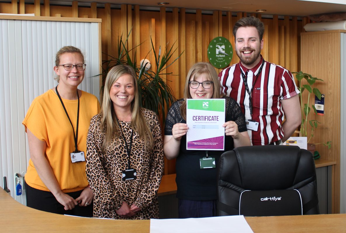 Four people stood behind a reception desk, one with a certificate celebrating an award.
