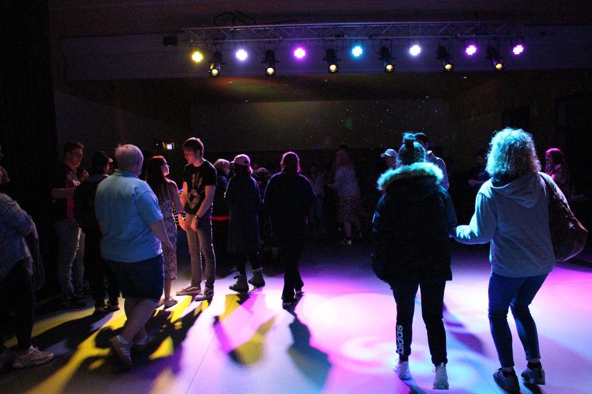 A group of people in a darkened space with disco lights shining at the Friday Club Night.