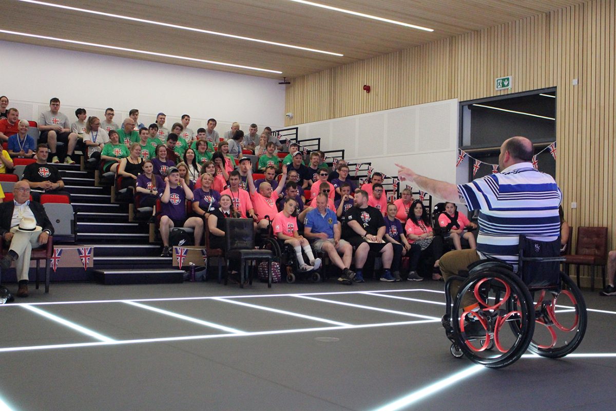 Man in wheelchair addressing an audience of many people.