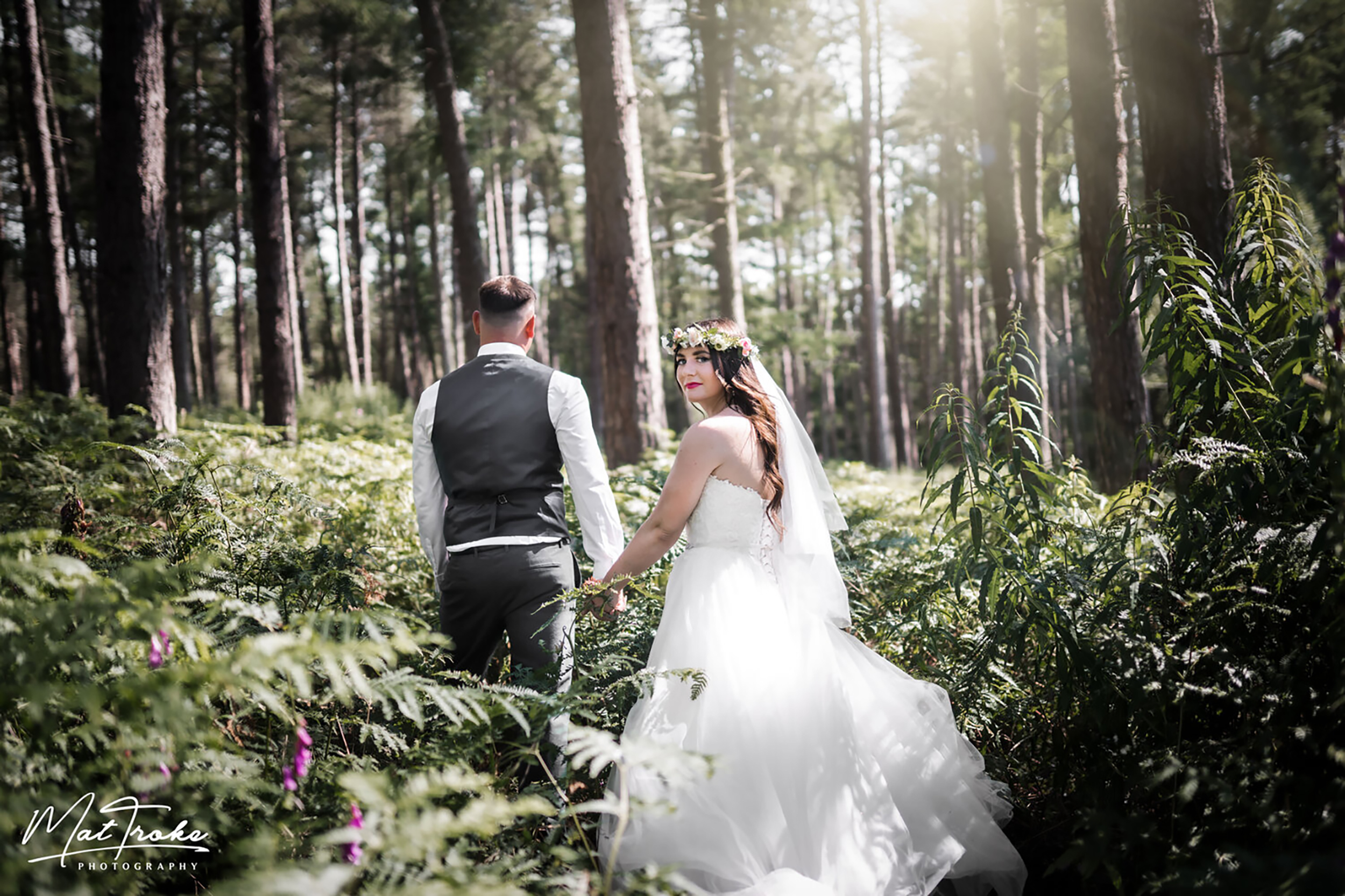 A bride and groom in a forest surrounded by bracken.