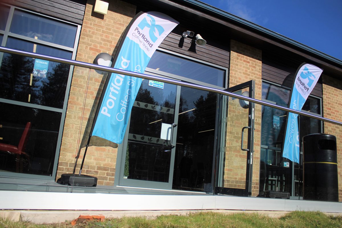 The entrance of the Portland Coffee Shop with tall blue flags on either side of the entrance,