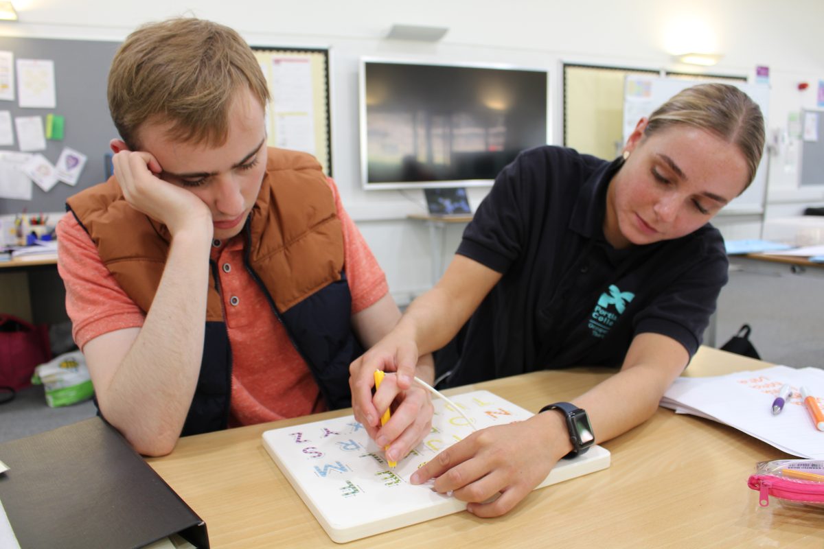 Occupational therapist helping a male learner with holding a pen and writing
