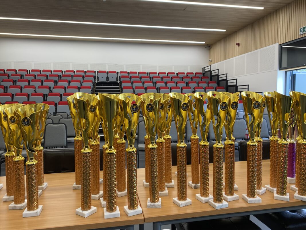 Close up image of gold trophies on a table with bleacher seating in the background
