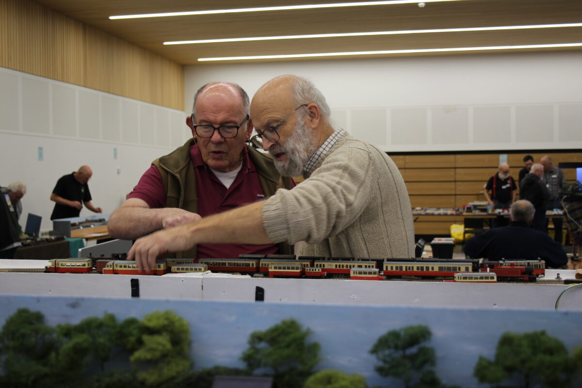 Image of two middle aged men with classes looking at a model train set