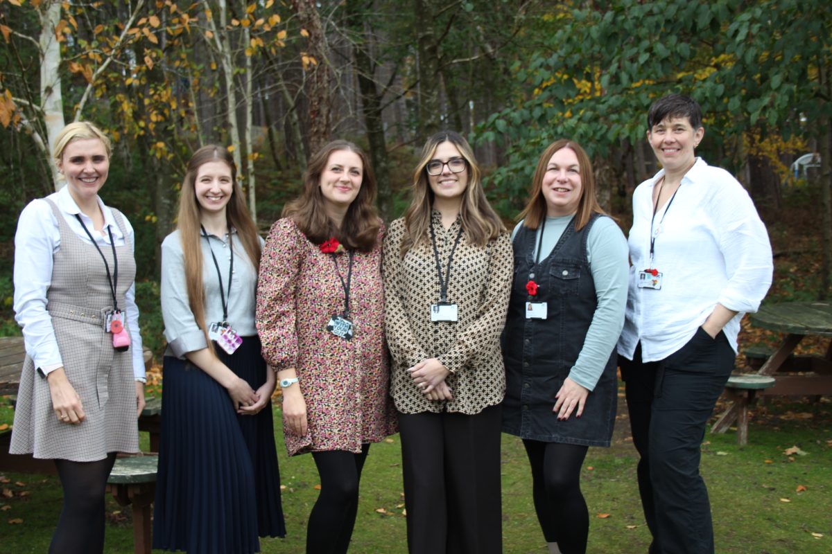 A group of five people standing in a row looking at the camera and smiling