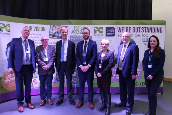 group of men and women dressed in suits, stood in front of a backdrop