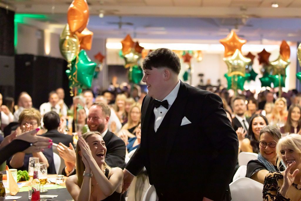 a crowd full of people cheering for smiling man wearing black suit
