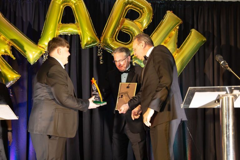three men wearing black suits, smiling during an award exchange