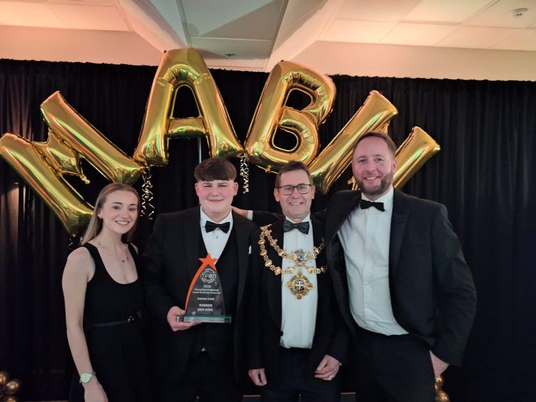 A smiling group photo with three men in black tie suits and one blonde female in a black dress