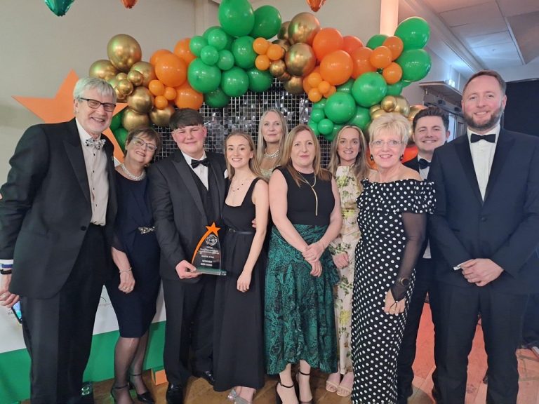 A group of 11 men and women dressed in suits and dresses, smiling with an award
