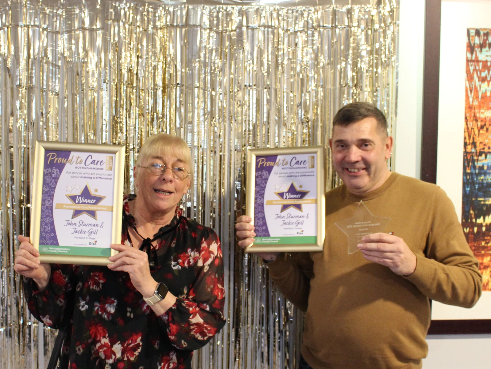 A male and female smiling while holding up two framed certificates.