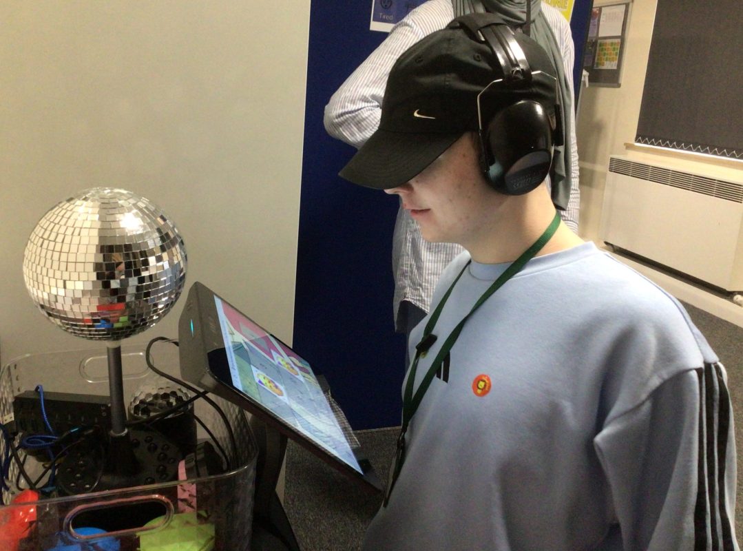 A male wearing a blue jumper and black cap while using a robot