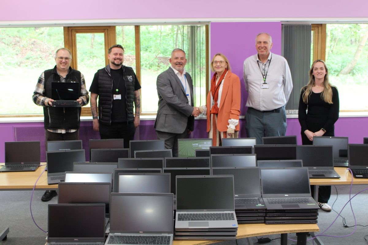 four men and two women smiling in front of 100 laptops