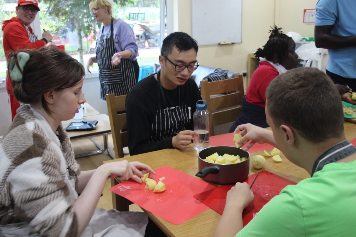 male wearing green top, male wearing a black sweatshirt and female wearing checkered jacket, cooking together