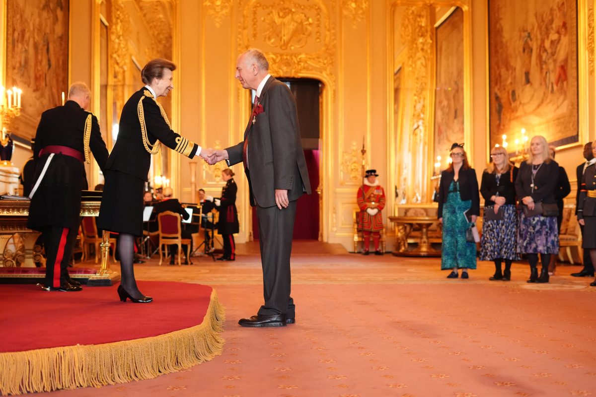 Older man wearing a grey suit shaking hands with an older princess in the Windsor Castle